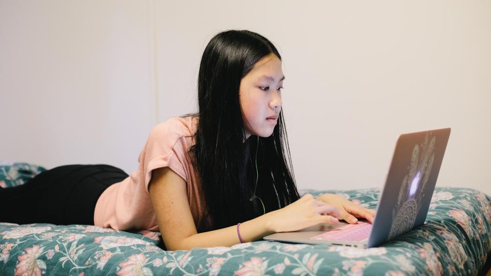 A participant lays on her bed, typing on her computer.